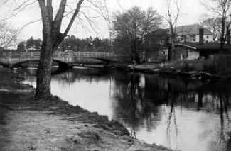 black & white photo of creek with house and bridge